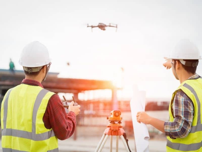 Land surveyors using drone and GPS equipment to document property conditions before road and infrastructure construction projects begin.