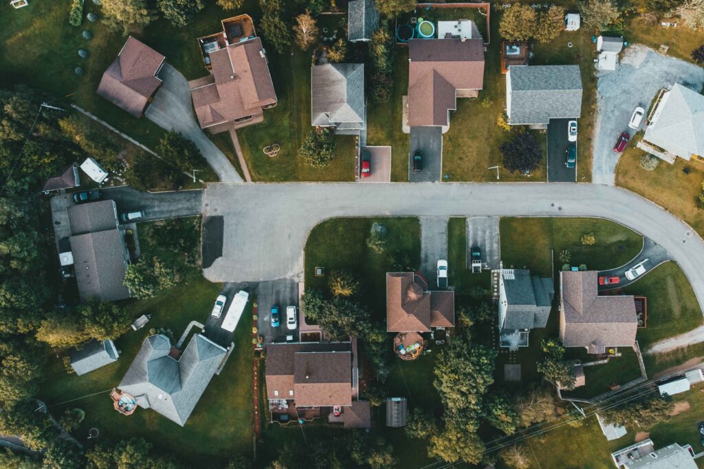 Aerial view of a suburban neighborhood showing houses, driveways, lawns, and winding streets with several parked cars suburban cul-de-sac pattern.